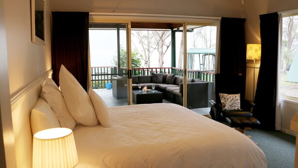 A hotel room with a large bed, a sofa, a small table with glasses and a candle, and a view of the outdoor balcony. - Absolute  luxury, surprising additions, welcome hamper & wine, cheese & biscuits (Hunter Valley)