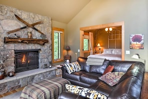 A cozy living room with a stone fireplace, leather sofa, and a wooden door leading to a bedroom.