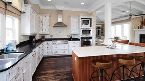 A spacious kitchen with white cabinetry, a large island with stools, and a built-in oven. - Gulf View, Large Home with Elevator, and Easy Beach Access ~ Sammys Old Place (Indian Pass)