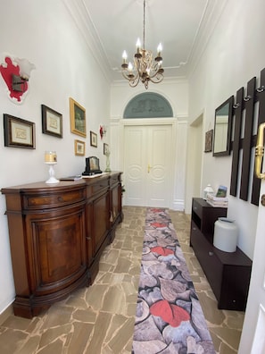 A hallway with a chandelier, a wooden cabinet, a stone-patterned carpet, and a white door. - A VALE OF HOUSE - for rural holiday accommodation (Pistoia)