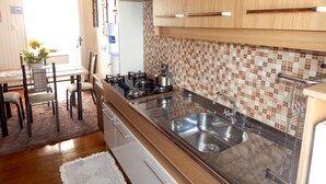 A compact kitchen with a gas stove, stainless steel sink, and wooden cabinets. - Casa Gramado Encantos (Gramado)