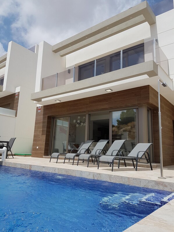 Un edificio moderno con piscina, sillones de descanso y puerta de acceso de vidrio.