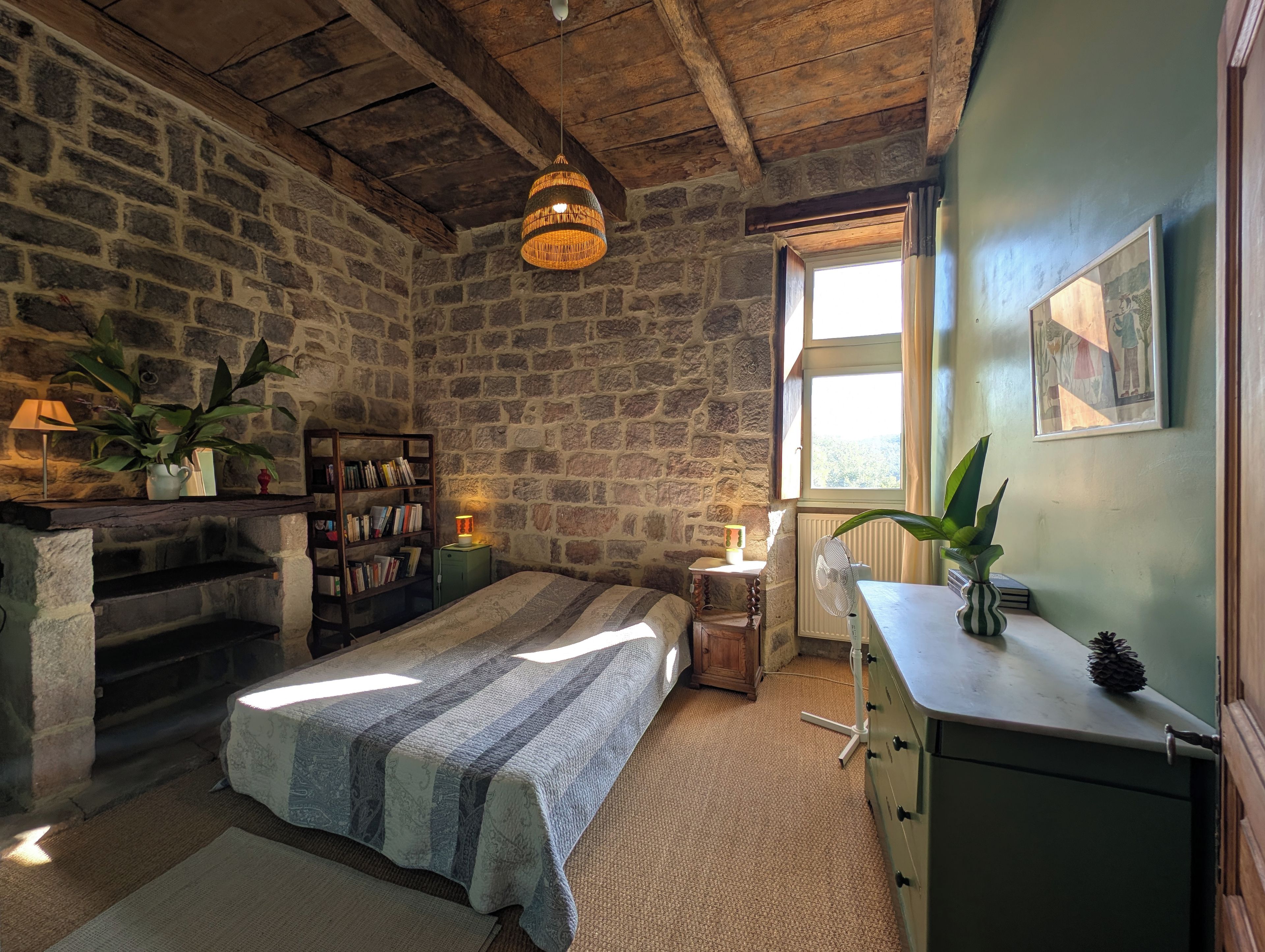 Een gezellige kamer met een stenen muur, een bed met een gestreept dekbed, een houten dressoir en een raam met daglicht.