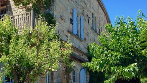 A stone building with a balcony, surrounded by greenery and flowers. - Renovated farmhouse of the 16th, charming, south Ardèche (Chassiers)