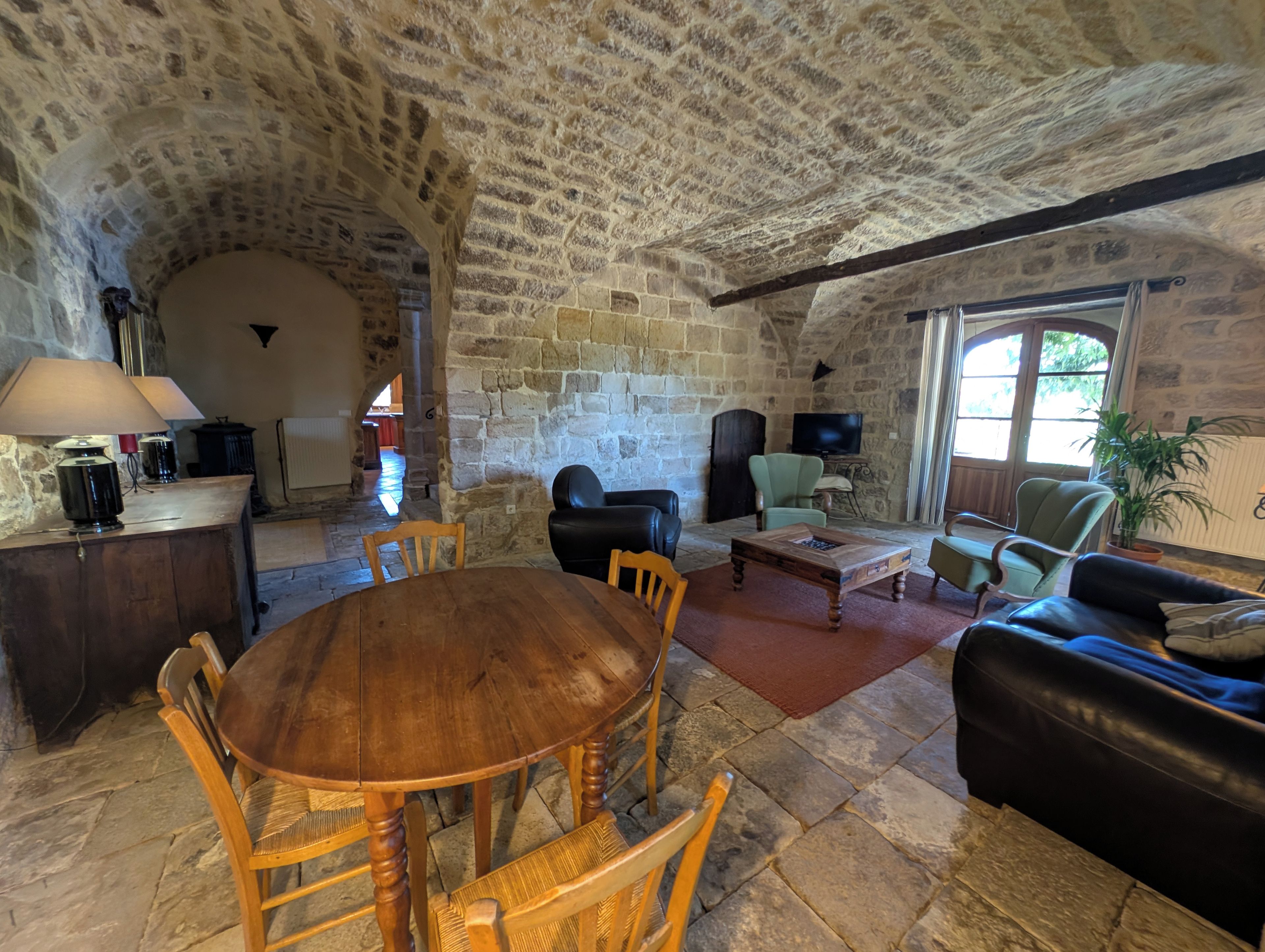 A stone-walled room with a round wooden table and chairs, a sofa, and a television.