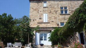 A stone building with a white door and windows, outdoor seating, and potted plants. - Renovated farmhouse of the 16th, charming, south Ardèche (Chassiers)