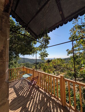 A wooden deck with a table and chairs, overlooking a forested landscape.