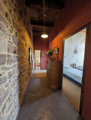 A narrow hallway with stone walls, a wooden cabinet, and a bed with a canopy.