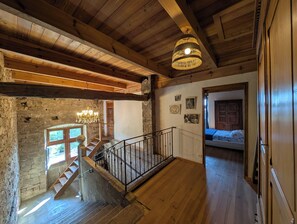 Un escalier en bois avec une rampe, un lustre et des murs en pierre.