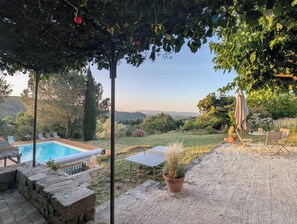 Un espace piscine avec vue sur la campagne, une table avec des chaises et une plante en pot.