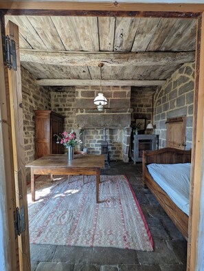 A rustic room with a stone wall, wooden ceiling, a bed, a table with a vase of flowers, and a fireplace. - Charming 16th-century country house, in Ardèche, with views of the Cévennes. (Chassiers)