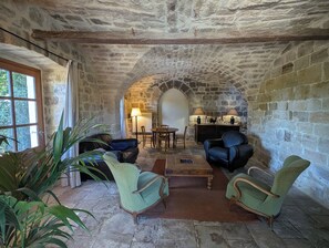 A stone-walled room with a fireplace, leather armchairs, a wooden coffee table, and a dining area with a table and chairs. - Charming 16th-century country house, in Ardèche, with views of the Cévennes. (Chassiers)