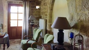 A rustic stone-walled room with a wooden door, a green armchair, a table with a lamp, and a radiator. - Renovated farmhouse of the 16th, charming, south Ardèche (Chassiers)