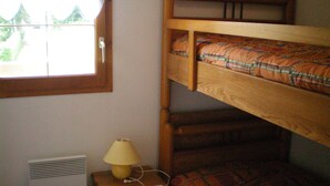 Un lit superposé avec un matelas à motifs, une table de chevet avec une lampe et une fenêtre donnant sur un paysage verdoyant.
