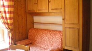 Une petite pièce avec un meuble en bois, un canapé à motifs et une table avec une chaise.