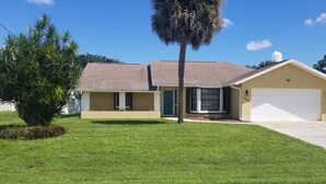 A single-story house with a beige exterior, a brown roof, and a white garage door.