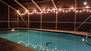 An indoor swimming pool with a clear water surface, surrounded by a tiled deck and a covered area with string lights.