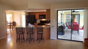 A modern kitchen with a central island, bar stools, and a dining area with wooden chairs.