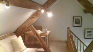 A cozy attic bedroom with a wooden beam ceiling, a white sofa, and a dining table with chairs. - Luxury Barn nr. Gastro-pub & Lake. Ideal Base for Hay, Ludlow, Hereford.Sleeps 4 (Titley, nr. Kington)