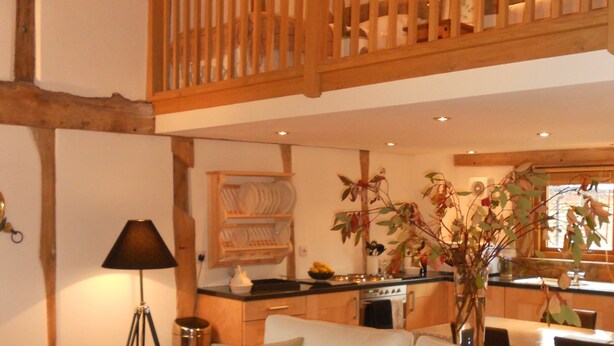 A spacious living room with a white sofa, a wooden ceiling, and a kitchen in the background. - Luxury Barn nr. Gastro-pub & Lake. Ideal Base for Hay, Ludlow, Hereford.Sleeps 4 (Titley, nr. Kington)