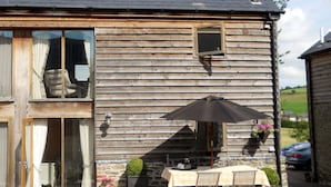 A wooden building with a window, a table with chairs, and a small umbrella. - Luxury Barn nr. Gastro-pub & Lake. Ideal Base for Hay, Ludlow, Hereford.Sleeps 4 (Titley, nr. Kington)