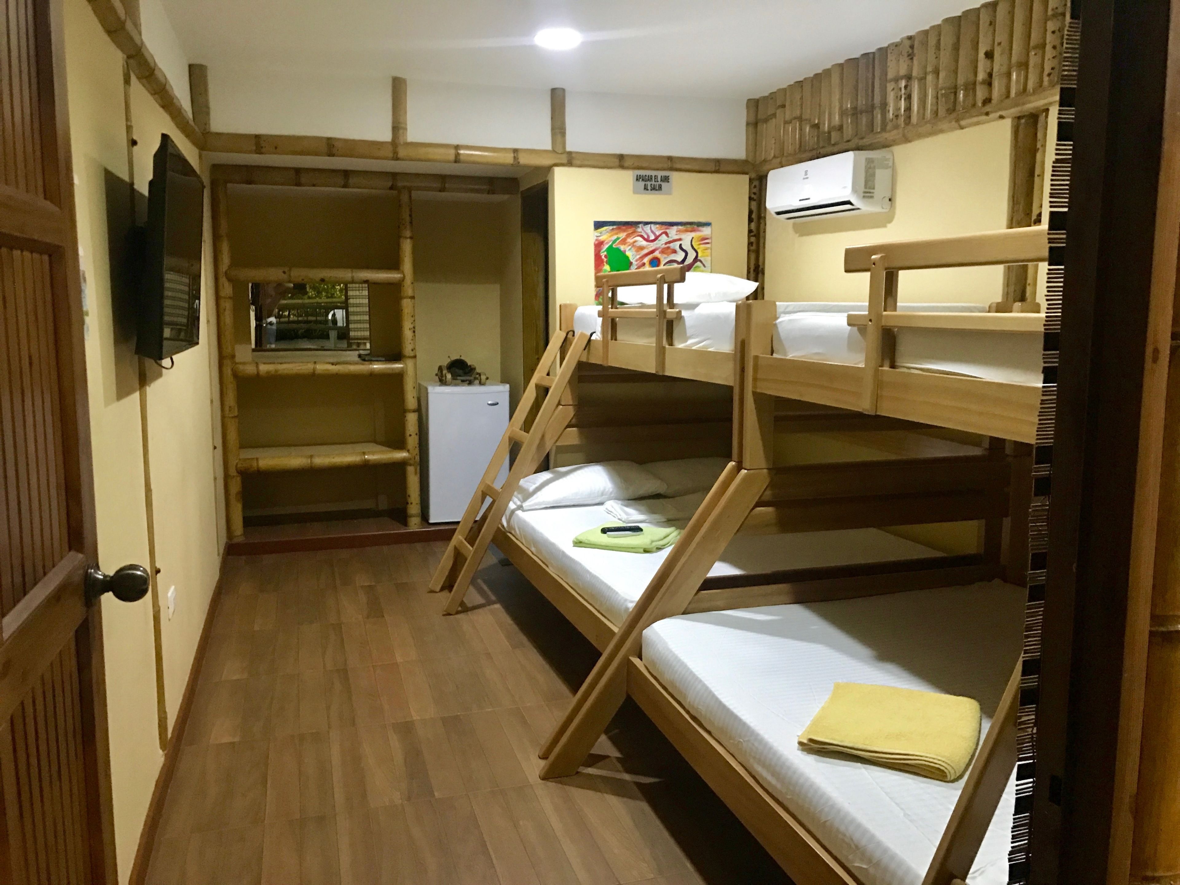 Quarto com beliche, piso de madeira, uma pequena geladeira branca e um quadro na parede.