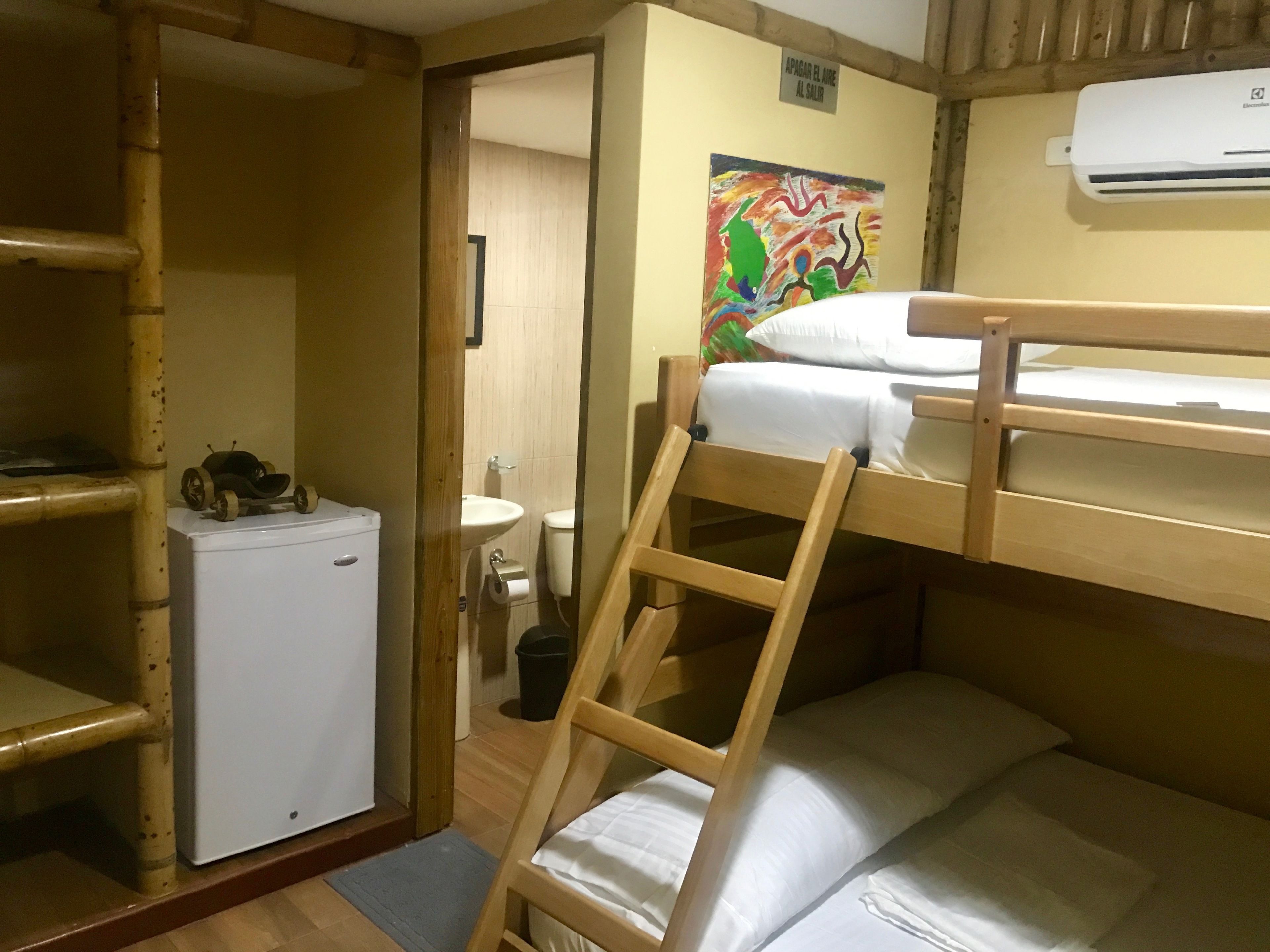 Ein kleines Zimmer mit Etagenbett, kleinem Kühlschrank, Spüle und einem farbenfrohen Bild an der Wand.