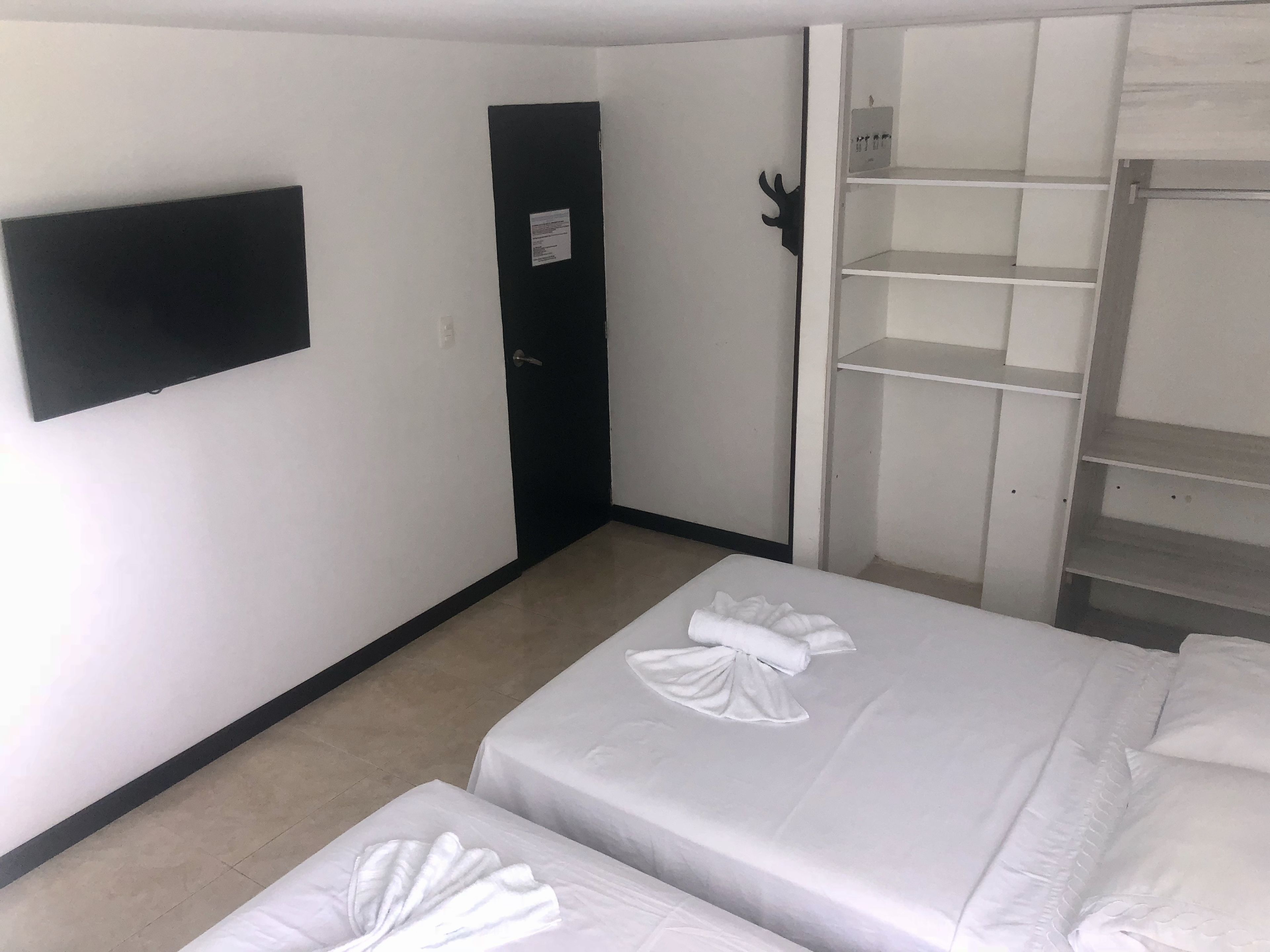 Ein Hotelzimmer mit zwei Betten, einem an der Wand befestigten Fernseher, einem Kleiderschrank und einer Tür.