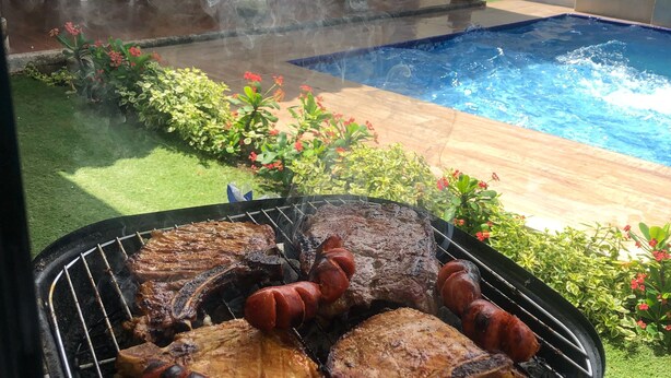 A backyard with a pool, a grill with meat, and a patio area. - Apartamentos Martinez (San Andrés)