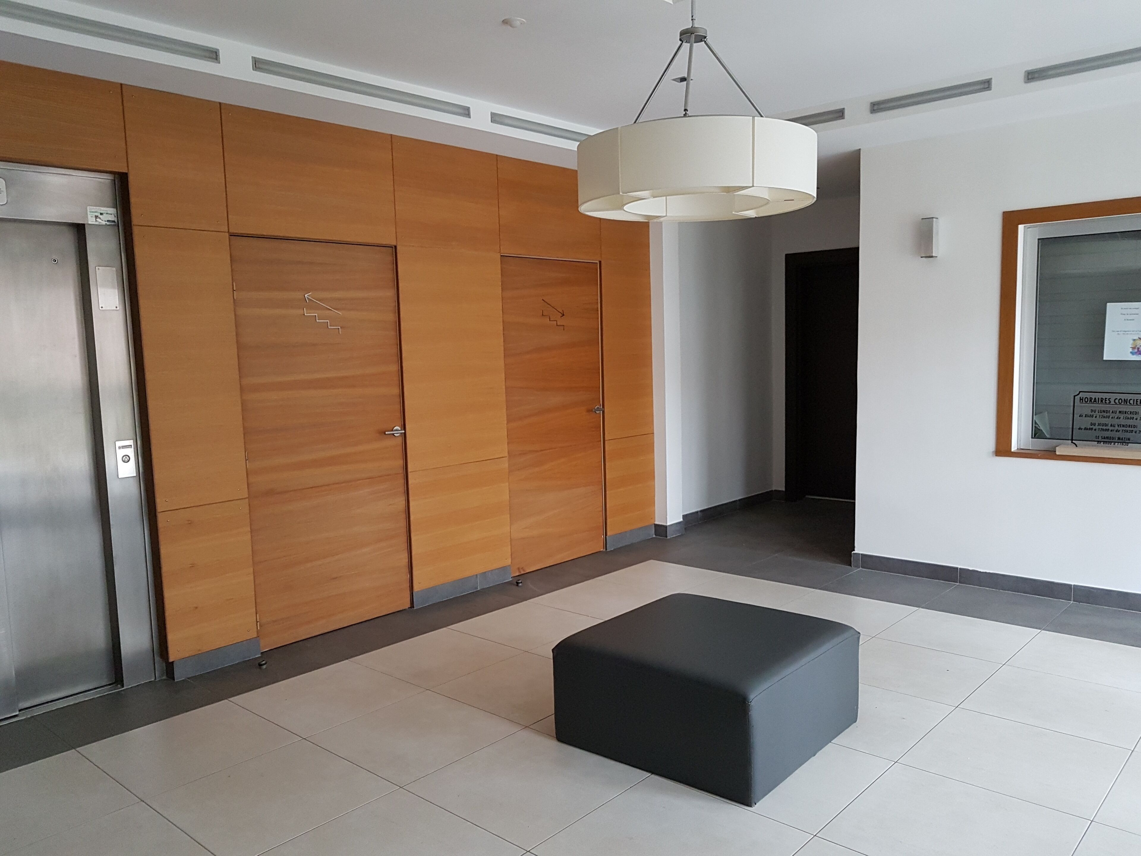 Un intérieur moderne avec un lambris en bois, un pouf noir et un luminaire suspendu au plafond.