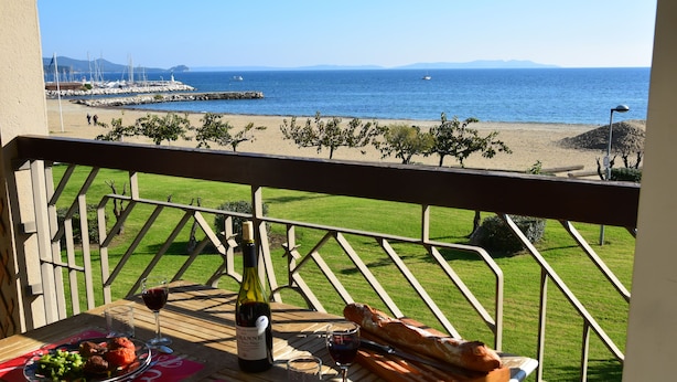 Un balcón con una mesa lista para una comida, con vista a la playa y al mar.