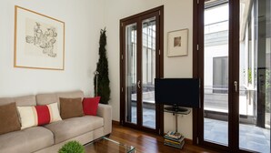 A living room with a sofa, a glass coffee table, a TV on a stand, a framed picture on the wall, and a tall plant. - Corral del Rey Terraza Sevilla Duplex, chillout terrace (Sevilla)