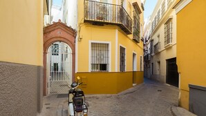 A narrow cobblestone street with a yellow building on the right and a white building on the left. A scooter is parked in front of the yellow building. - Corral del Rey Terraza Sevilla Duplex, chillout terrace (Sevilla)
