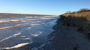Une plage avec des vagues, un ciel dégagé et une falaise herbeuse.