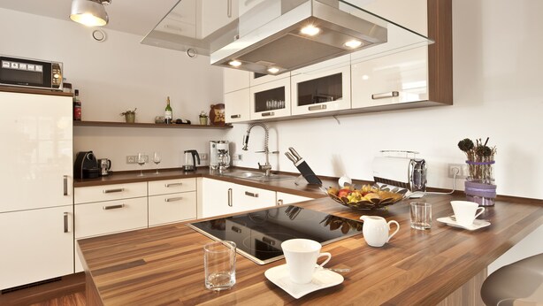 Une cuisine moderne avec des meubles blancs, un plan de travail en bois et une plaque de cuisson à induction intégrée.