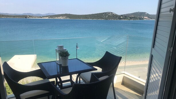 Ein Balkon mit Tisch und Stühlen mit Blick auf ein klares, blaues Meer und eine entfernte Küste.