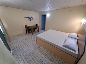 A small, clean room with a single bed, a table with chairs, and a fan on the wall. - Fun World Plaza Hotel (Nadi)