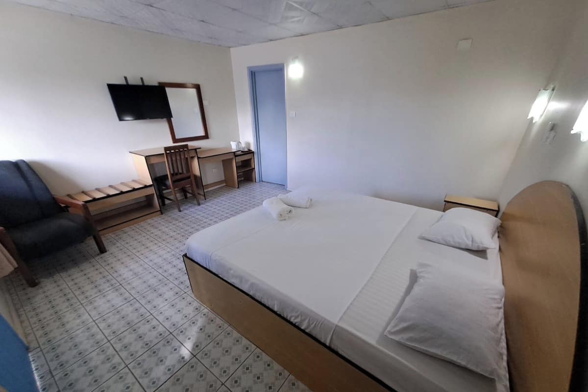 Una habitación de hotel con cama, escritorio, silla y televisión en la pared.