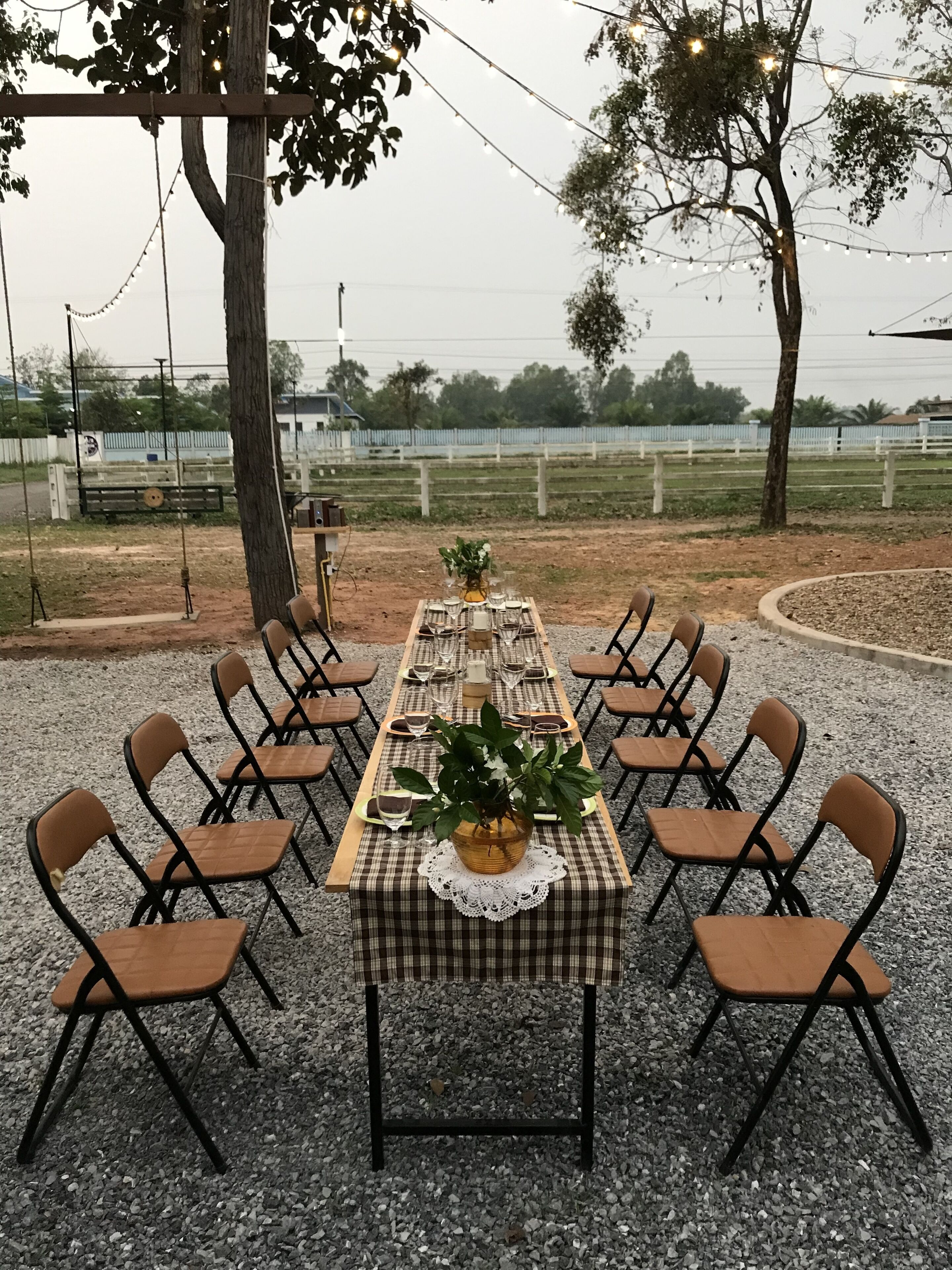 An outdoor dining area with a long table set for six, surrounded by chairs, under string lights.