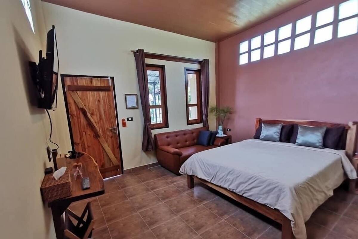 Une chambre à coucher avec un lit, un bureau en bois, une télévision et une fenêtre avec des rideaux.