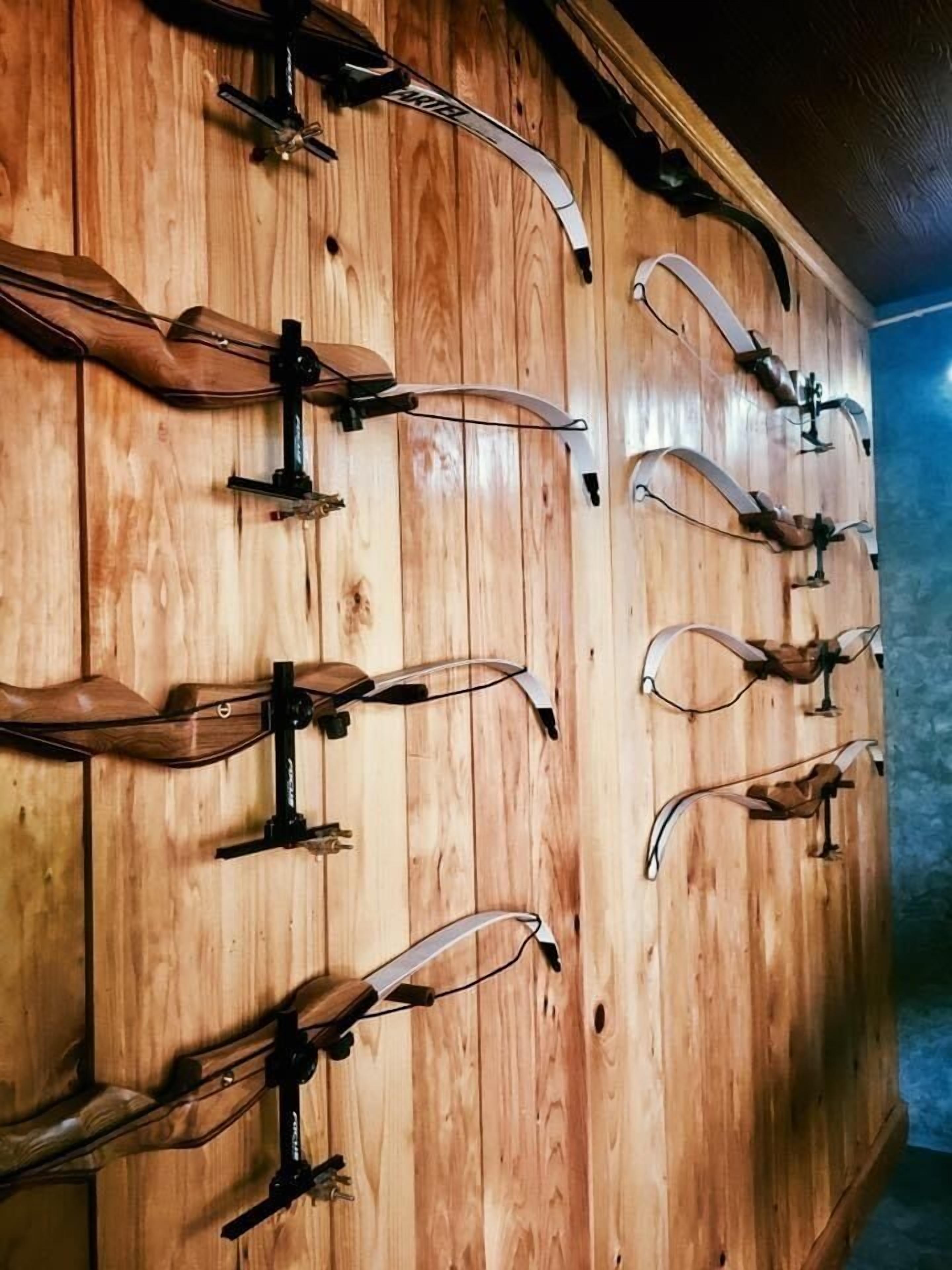 A wooden wall with multiple archery bows mounted on it.