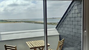 A balcony with a view of a calm body of water, a sandy beach, and a distant shoreline. There are wooden chairs and a table on the balcony. -  MORBIHAN - SPLENDID VIEW ON THE RIA AND THE BAR OF ETEL - 15 METERS FROM THE BEACH  (Étel)