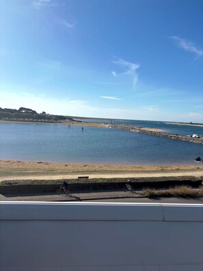 Une vue sur la côte, avec un ciel dégagé, une plage de sable et une digue rocheuse.