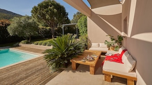 Een zwembadterras met een houten dek, een ligstoel, een bijzettafeltje met dienblad en een pergola.
