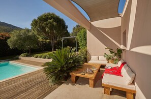A poolside area with a wooden deck, a lounge chair, a small table with a tray, and a pergola.