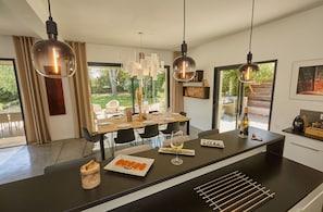 A modern kitchen with a central island, pendant lights, and a dining area with a view of the outdoors. - Villa Malona des Albères in Sorède 7 km from the beaches (Sorède)