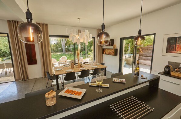A modern kitchen with a central island, pendant lights, and a dining area with a view of the outdoors.