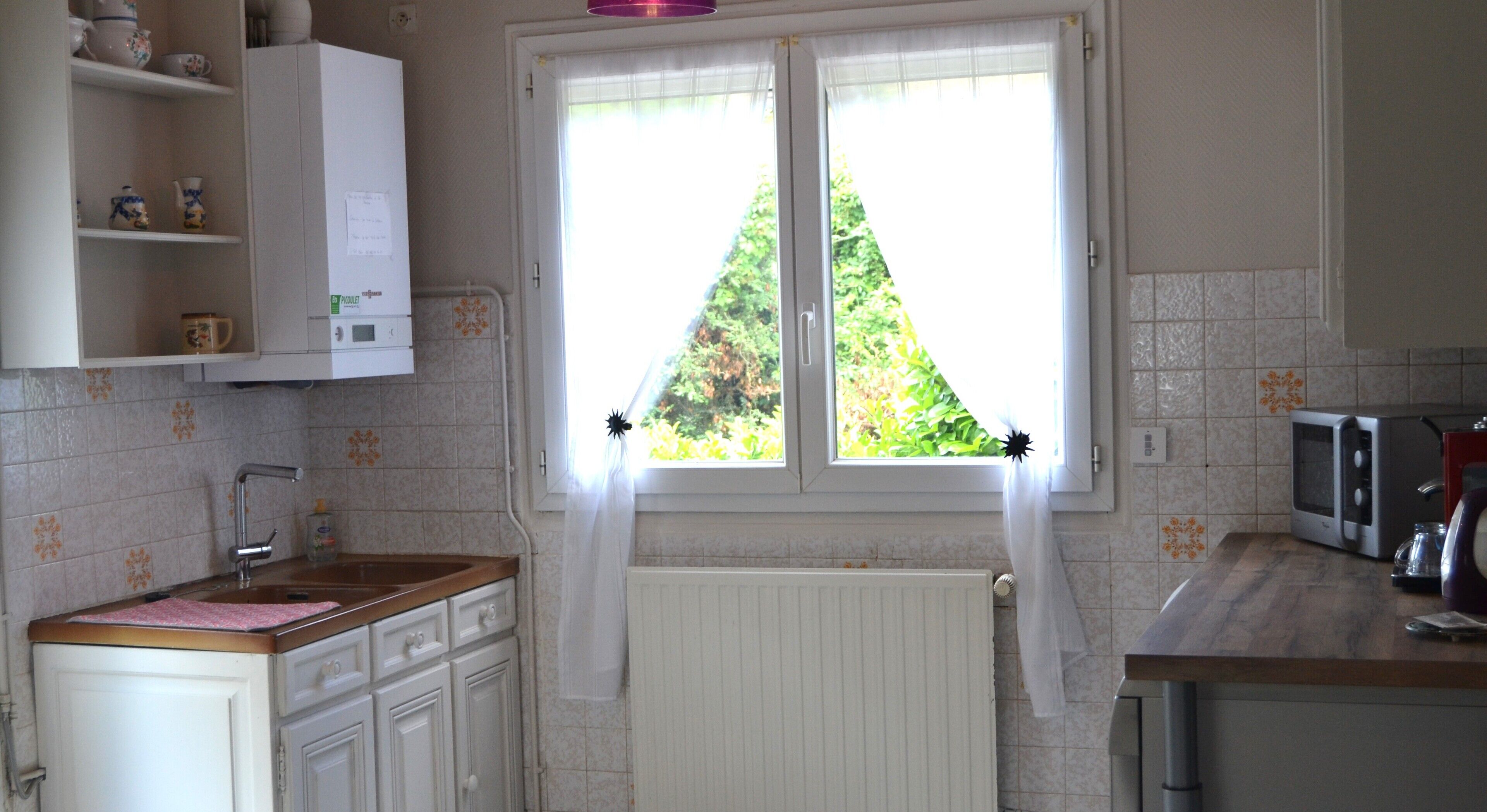 A kitchen with white cabinets, a wooden countertop, a window with curtains, and a microwave.