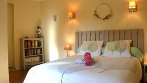 A bedroom with a bed, two wall-mounted lamps, a bookshelf, and a decorative wreath. - 3* Gîte l'ancienne Epicerie Meyronne (Meyronne)