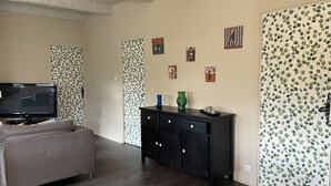 A living room with a grey sofa, a black entertainment unit, and a television. There are four framed artworks on the wall. - 3* Gîte l'ancienne Epicerie Meyronne (Meyronne)